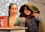 Chuck wears his cloak and gestures next to Agness who is seated at a desk in a scene from the play She Kills Monsters