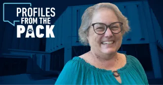 Image of Cathy Hare in a blue shirt smiling. A Profiles from the Pack logo with the exterior of the Commercial Avenue campus building is in the background.