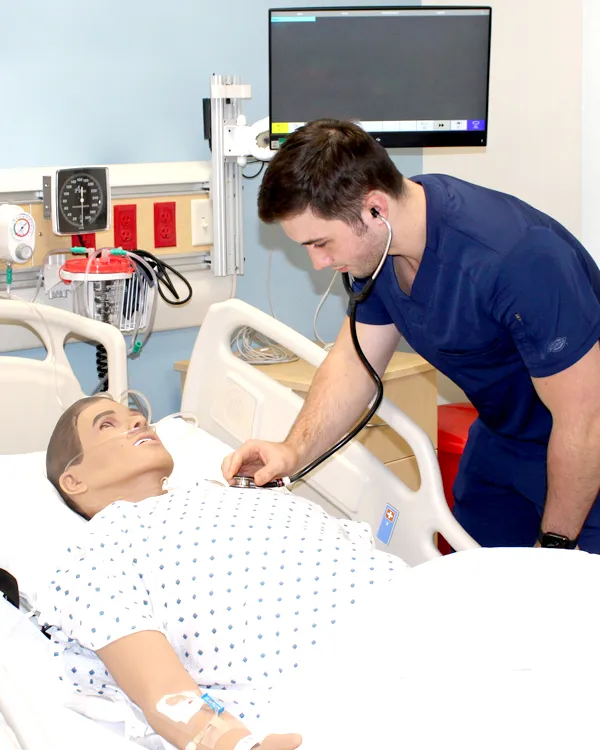 Student using a stethoscope on a manikin in a Watertown Nursing lab